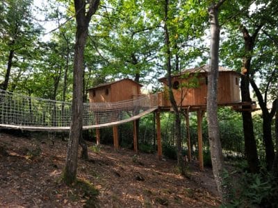 Cabane perchée dans les arbres, reliée par un pont en filet, au cœur de la nature.
