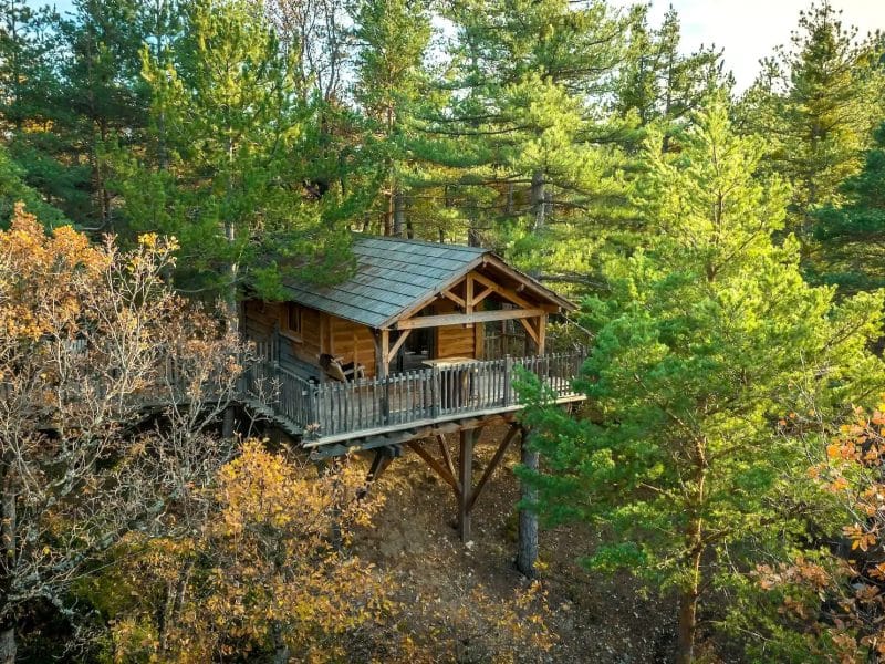 Cabane dans les arbres entourée de feuillage automnal, offrant une vue paisible.
