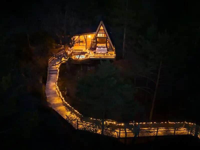 Cabane en bois illuminée, entourée de nature, avec un chemin lumineux.