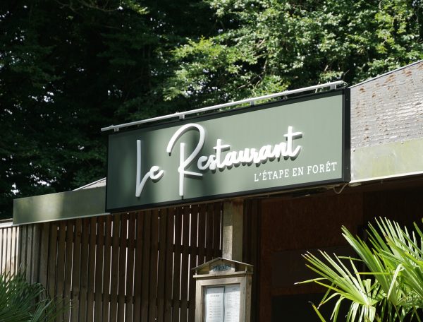 Restaurant LÉtape en Forêt avec une belle enseigne en bois et verdure environnante.