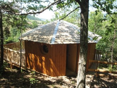 Cabane en bois perchée, toit en pente, entourée darbres verdoyants en Auvergne.