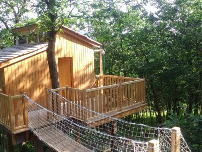 Cabane perchée en bois avec terrasse, entourée darbres verdoyants en Auvergne.
