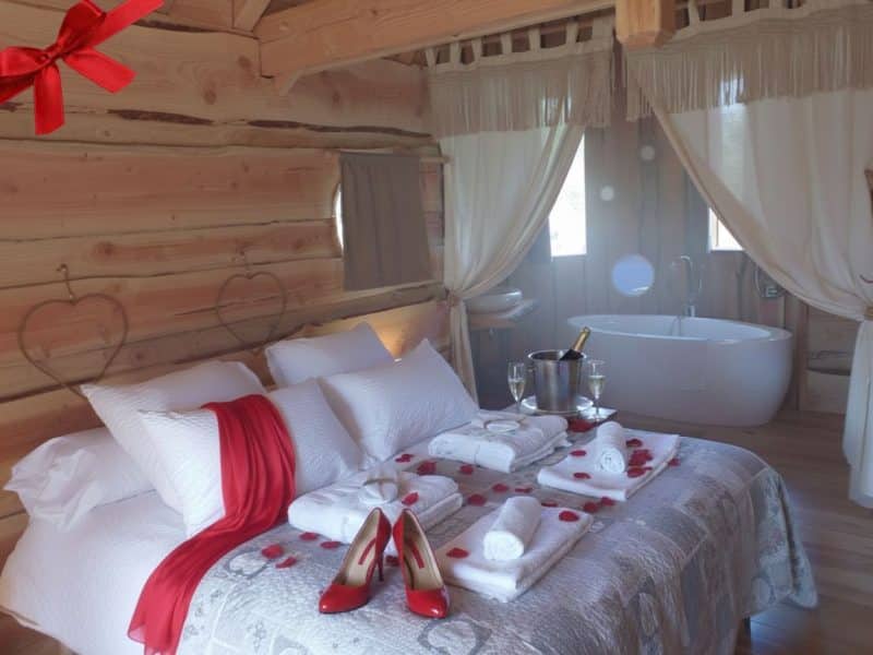 Chalet romantique avec lit douillet, baignoire et décor chaleureux en bois.