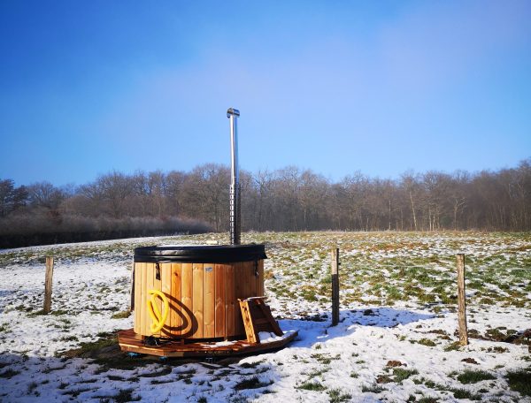 Hébergement insolite : un sauna en bois au milieu dun champ enneigé sous un ciel bleu.