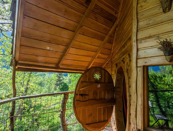 Cabane en bois perchée, avec une terrasse en bois et une vue sur la forêt verdoyante.