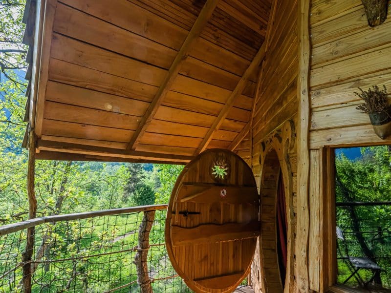 Cabane en bois perchée, avec une terrasse en bois et une vue sur la forêt verdoyante.