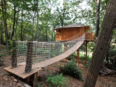 Cabane dans les arbres en Auvergne-Rhône-Alpes, accessible par un pont suspendu.