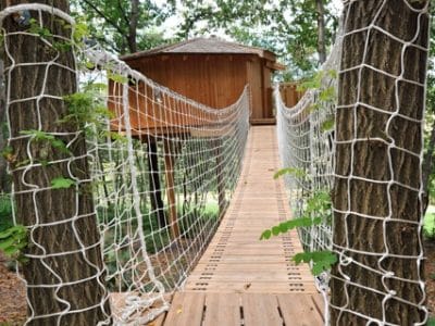 Cabane dans les arbres en Auvergne, accessible par un pont suspendu en bois.