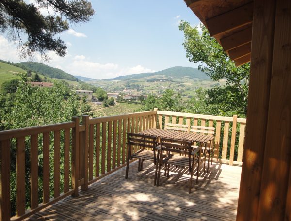 Chalet en bois avec terrasse, vue panoramique sur les collines verdoyantes.