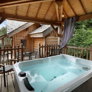 Chalet en bois avec jacuzzi sur la terrasse, entouré de verdure apaisante.