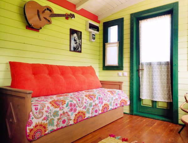 Chalet coloré avec un canapé fleuri et une guitare accrochée au mur.