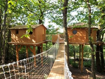 Cabane dans les arbres en Auvergne-Rhône-Alpes, reliée par un pont en bois.