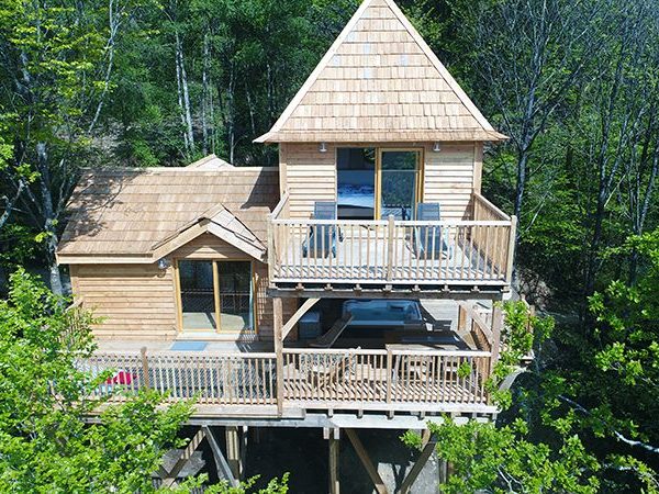 Cabane en bois perchée dans les arbres, avec balcon et vue sur la forêt.