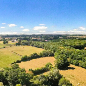 Vue panoramique dun gîte rural entouré de verdure et de champs ensoleillés.