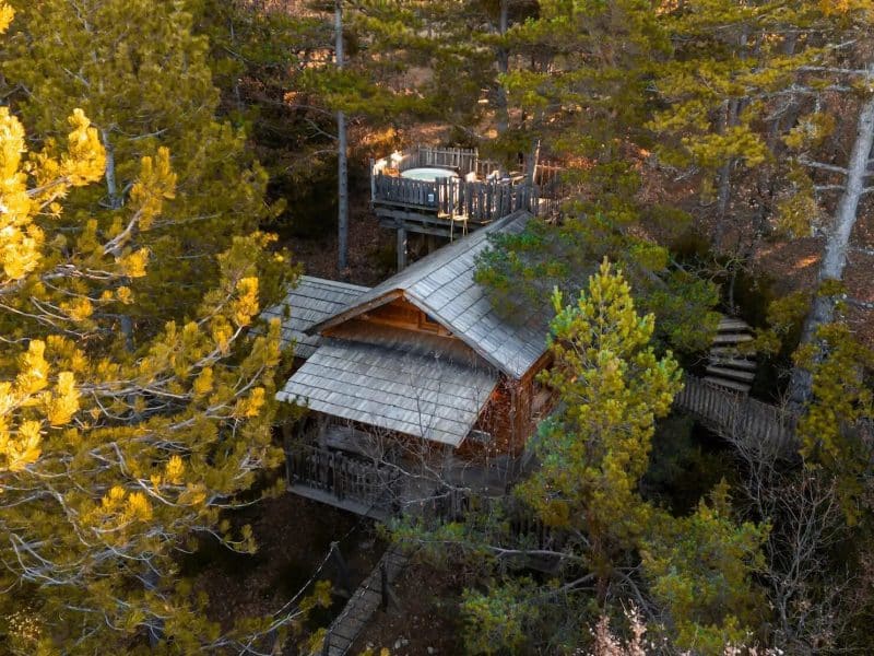 Cabane en bois nichée parmi les arbres, avec une terrasse en bois surplombante.