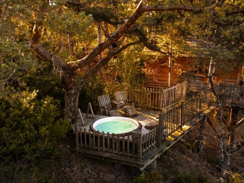Cabane perchée avec jacuzzi sur une terrasse entourée darbres.