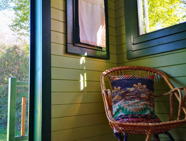 Cabane en bois avec une chaise en rotin et lumière naturelle filtrant par les fenêtres.