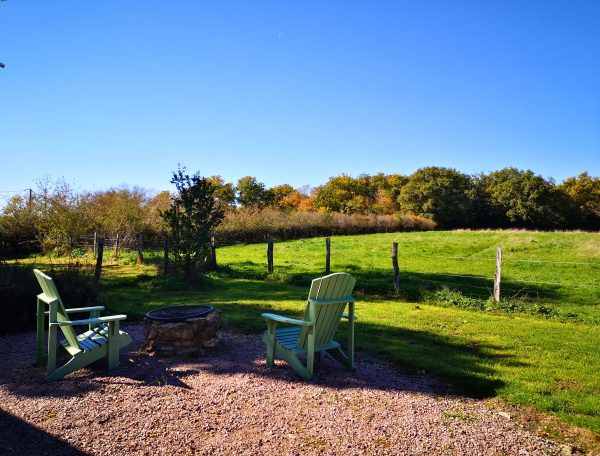 Chalet en pleine nature avec chaises Adirondack et vue sur un champ verdoyant.