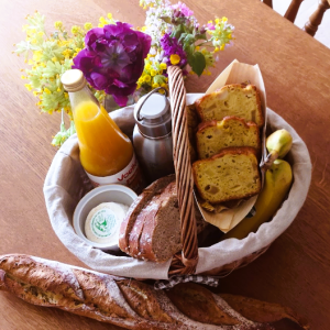 Panier gourmand dans un gîte, avec pain, jus et fleurs colorées.