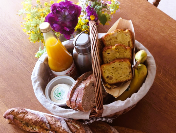 Panier gourmand dans un gîte, avec pain, jus et fleurs colorées.