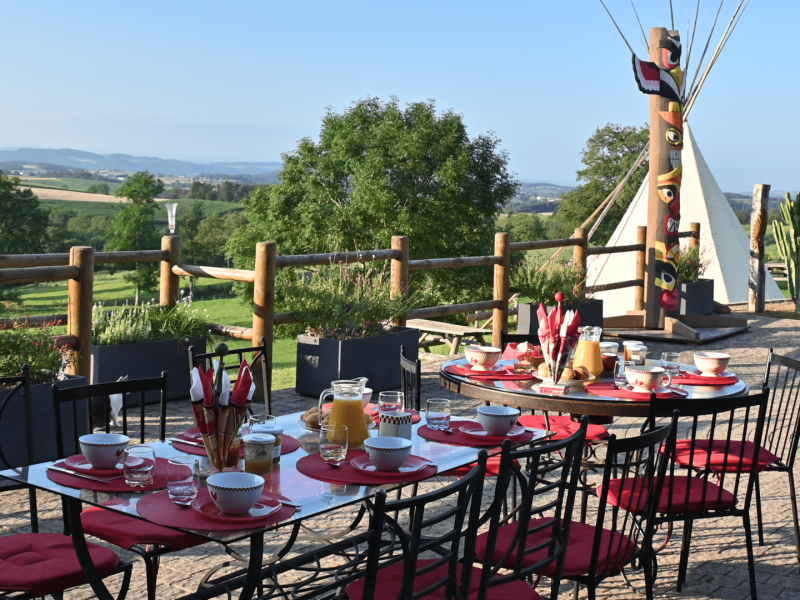 Tentes tipis avec vue panoramique, table dressée pour un petit-déjeuner en plein air.