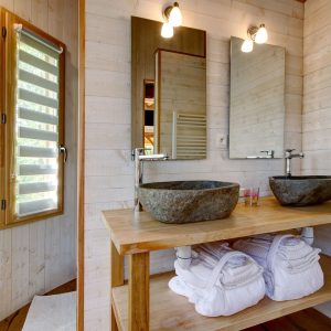 Salle de bain moderne en bois avec vasques en pierre dans un hébergement insolite en Bretagne.