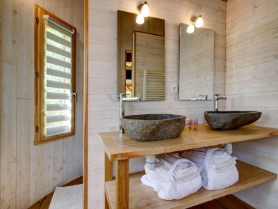Salle de bain moderne en bois avec vasques en pierre dans un hébergement insolite en Bretagne.