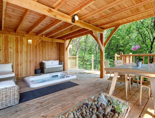 Chalet en bois avec jacuzzi, terrasse en bois entourée de verdure.