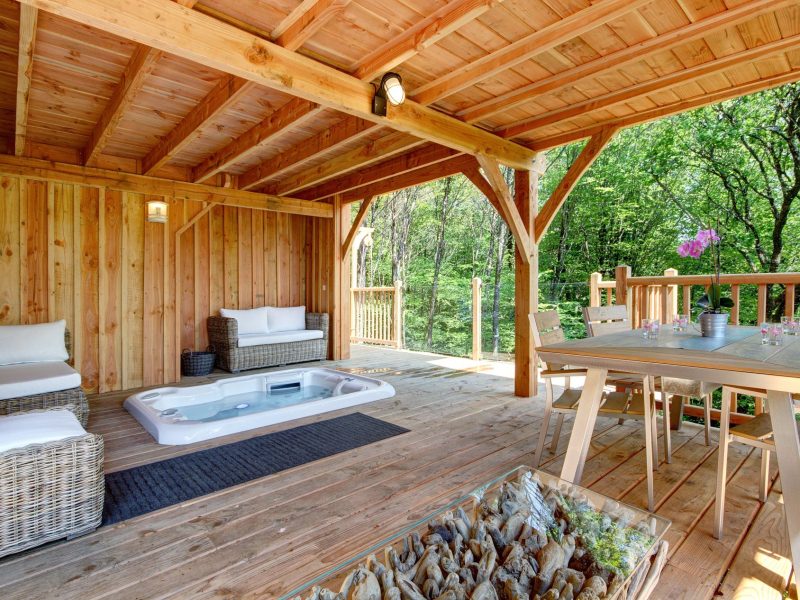 Chalet en bois avec jacuzzi, terrasse en bois entourée de verdure.