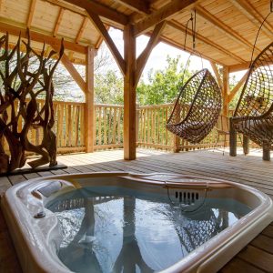 Cabane perchée en Bretagne avec jacuzzi et chaises suspendues en osier.