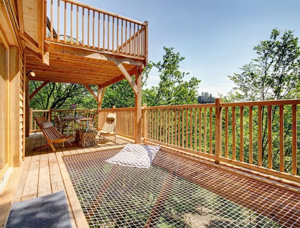Cabane perchée avec terrasse en bois et hamac, entourée darbres verdoyants.