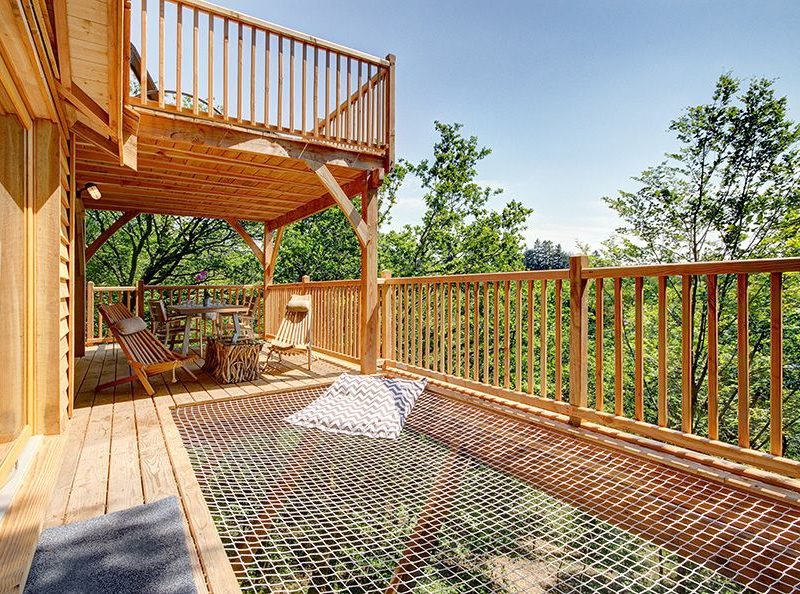 Cabane perchée avec terrasse en bois et hamac, entourée darbres verdoyants.