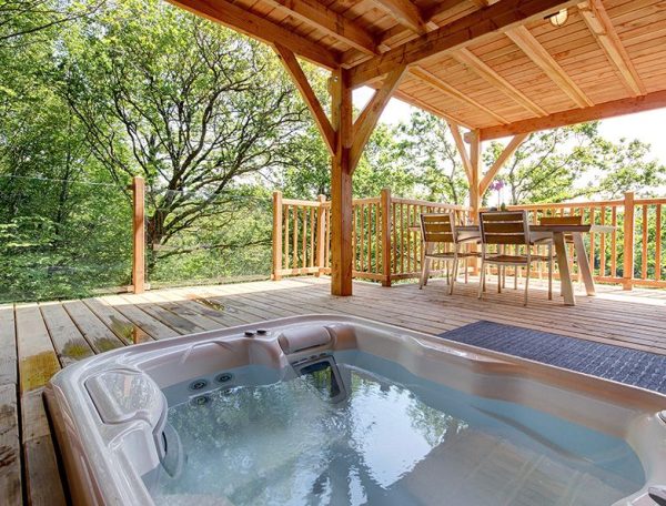 Chalet en bois avec jacuzzi sur la terrasse, entouré de verdure.
