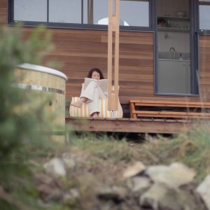 Chalet moderne en bois avec terrasse, une femme lit paisiblement.