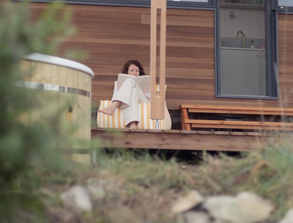 Chalet moderne en bois avec terrasse, une femme lit paisiblement.