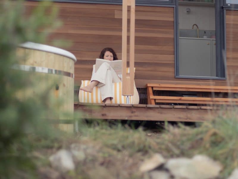 Chalet moderne en bois avec terrasse, une femme lit paisiblement.