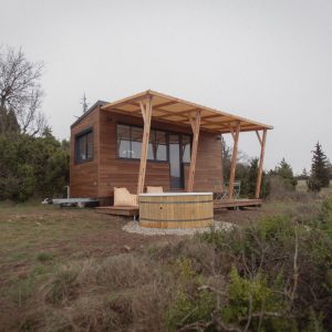 Chalet en bois avec terrasse, entouré de verdure et dun jacuzzi extérieur.