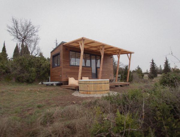 Chalet en bois avec terrasse, entouré de verdure et dun jacuzzi extérieur.