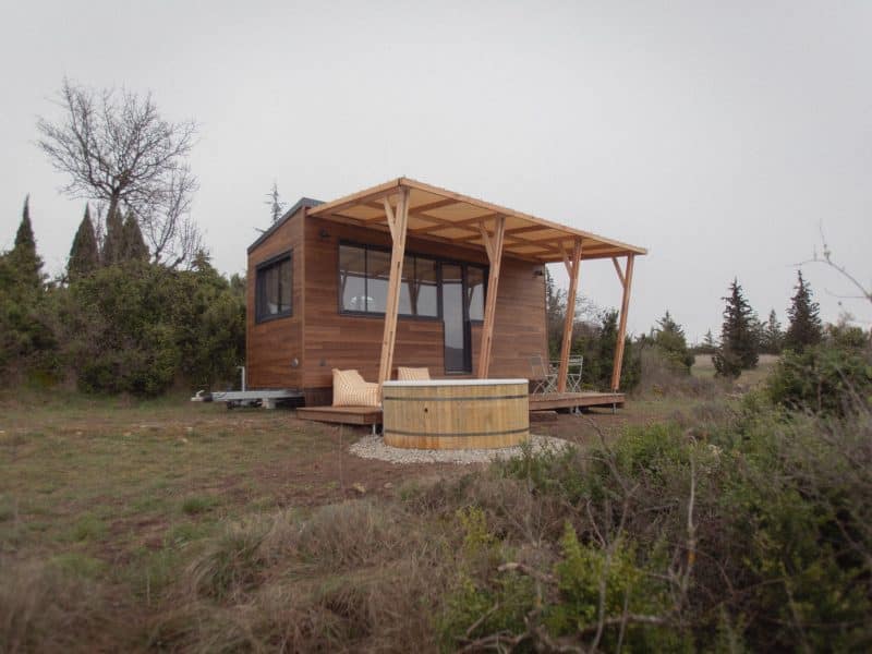 Chalet en bois avec terrasse, entouré de verdure et dun jacuzzi extérieur.