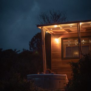 Cabane en bois avec jacuzzi extérieur, éclairage doux au crépuscule.