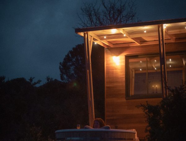 Cabane en bois avec jacuzzi extérieur, éclairage doux au crépuscule.