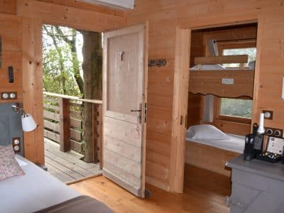 Cabane en bois dans les arbres, avec un balcon et des lits superposés.