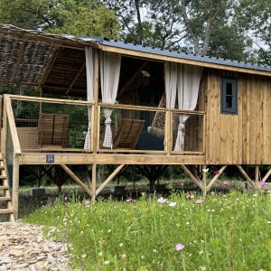 Cabane en bois sur pilotis, entourée de fleurs colorées et dune terrasse accueillante.