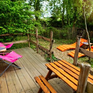 Hébergement insolite en cabane avec terrasse en bois et chaises colorées.
