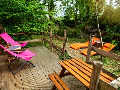 Hébergement insolite en cabane avec terrasse en bois et chaises colorées.