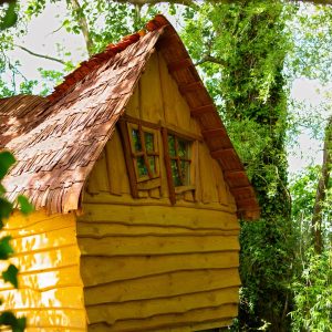 Cabane en bois perchée, toit en ardoise, entourée de verdure luxuriante.