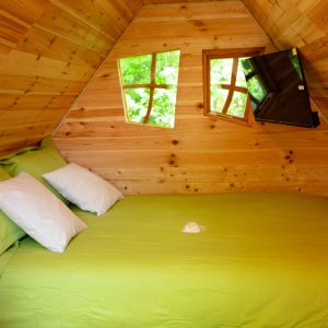 Cabane en bois avec lit double et fenêtres en forme de croix, ambiance chaleureuse.