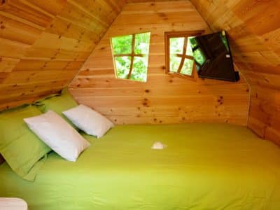 Cabane en bois avec lit double et fenêtres en forme de croix, ambiance chaleureuse.