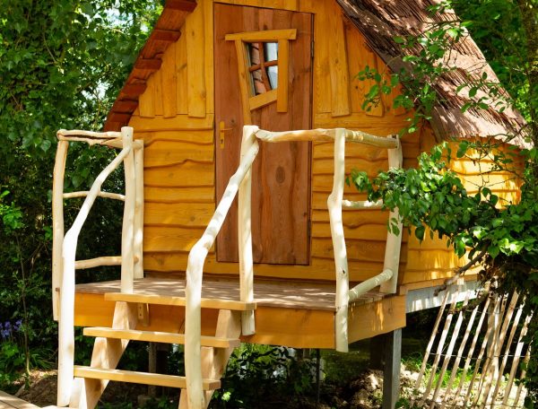 Charmante cabane en bois avec un balcon, entourée de verdure et un chien au repos.