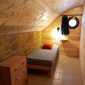 Chalet en bois en Auvergne, avec un lit simple et une fenêtre ronde.